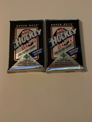 NHL Hockey 1990-91 samlarkort - Två oöppnade paket NHL Hockey samlarkort från Upper Deck, säsongen 1990-91. Varje paket innehåller 12 kort och är märkta som Premiere Edition. Förpackningarna är svarta med inslag av silver, blått, rött och grönt.