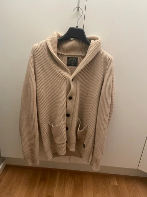 Beige stickad kofta från Jack & Jones L - Säljer en beige stickad kofta från Jack & Jones Vintage med knappar framtill och två stora fickor.