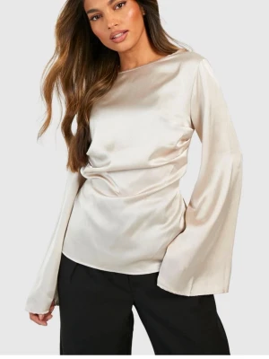 Champagnefärgad satintopp med vida ärmar - Snygg blus i glansigt satinmaterial med champagnefärg och rund halsringning. Modellen har långa, vida ärmar och en figurnära passform som ger en elegant look. Perfekt att styla med både jeans och kostymbyxor.