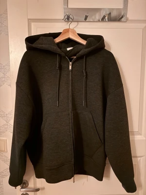 Zara zip hoodie - En stilren svart hoodie med dragkedja framtill, stor huva och dragsko. Hoodien har två rymliga fickor på magen och ribbade muddar vid ärmslut och nederkant. Perfekt för en avslappnad och cool look. S men passar M/L perfekt. 