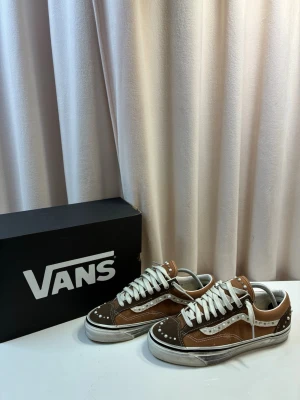 Vans LX Old Skool 36 pearlized sneakers - Snygga Vans Old Skool sneakers i brunt och vitt med coola nitar och detaljer. Skorna har klassisk låg profil, vit sula och vita skosnören. Ovandelen är i canvas och mocka, med den ikoniska Vans-sidan i vitt. Perfekta för en streetwear-look.