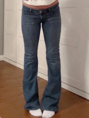 Blå bootcut jeans med låg midja - Snygga blå bootcut jeans med låg midja och klassiska fickor fram och bak. Jeansen har en lätt utsvängd passform nertill och stängs med knapp och dragkedja. Perfekta för en trendig och avslappnad look. Lite sliten vid slutet av ett ben men inget som syns.