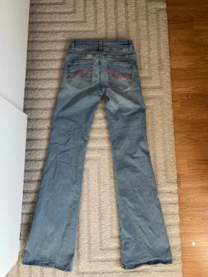 Ljusblå bootcut jeans Nelly - Ljusblå jeans med bootcut passform och broderade detaljer i rosa. Det är litet hål längst nere på jeansen på baksidan på ena benet men det är något man knappt ser