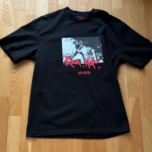 Boss Hugo T-shirt - Boss Hugo T-shirt i svart med rött logotryck och rockkonsert-motiv framtill. Loose fit med streetwear/rock-känsla, 