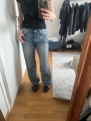 Blå raka jeans med hög midja - Säljer ett par klassiska blå jeans med rak passform och hög midja. Jeansen har fem fickor, bälteshällor och stängs med knapp och dragkedja. Perfekta till en avslappnad stil och passar till det mesta. Materialet är denim i bomull.