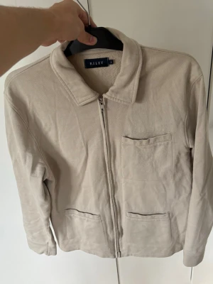Riley skjortjacka herr M - Superfin snygg beige skjortjacka från Riley högkvalitativ i storlek M säljes. Grym passform och väldigt prisvärd perfekt nu till sommaren! Inga hål eller fläckar och tveka inte vid minsta fråga eller fundering!