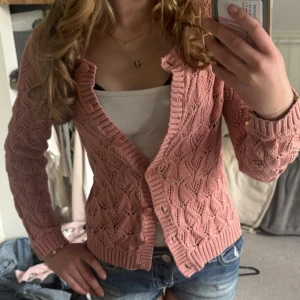 Rosa stickad kofta från Indiska - Söt rosa stickad kofta från Indiska med dekorativt hålmönster och ribbade kanter. Koftan har knappar framtill och gjord av 100% bomull. Hör av er om ni har frågor💕