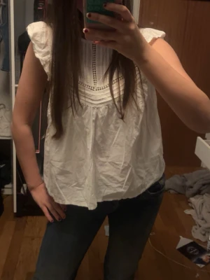 Vit volangblus med spetsdetaljer - Söt vit blus med volangärmar och dekorativa spetsdetaljer framtill. Blusen har en lös passform och fina veckade partier upptill. Perfekt för en fräsch och trendig look. Storlek 152 men passar mig okej som har S, knappt använd 