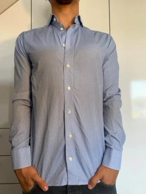 Blå mönstrad skjorta från Eton - Blå skjorta från Eton. Strl 38/ S. Inga defekter. Nypris runt 1200-2000kr. Modellen är 178 cm och väger 77 kg. Hör gärna av dig vid frågor!