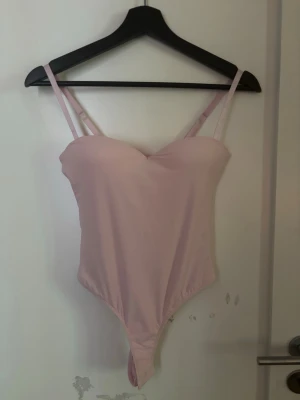 Ljusrosa body - Söt ljusrosa body med tunna, justerbara axelband och vadderade kupor. Bodyn har en enkel, stilren design och är gjord i ett mjukt, stretchigt material som sitter tajt mot kroppen. Perfekt med en kavaj över. Kan skicka mer bilder om man skulle vilja det. Storlek S men passar både xs och M så den är stretchig❤️