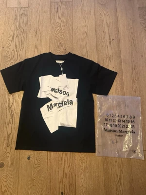 Maison Margiela svart t-shirt storlek M - Svart t-shirt från Maison Margiela med vit grafisk print och logga framtill. Klassisk passform med rund hals och korta ärmar. Tillverkad i mjuk bomull, perfekt för en trendig och avslappnad stil. Helt ny med tags pris kan diskuteras hör av er vid frågor 🤔