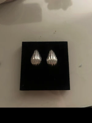 Silverfärgade droppformade örhängen - Snygga örhängen i droppformad design med räfflad yta i silverfärg. De har en stilren och modern look som passar perfekt till dig som gillar minimalistiska accessoarer. Materialet ser ut att vara metall och de är kompakta i modellen.