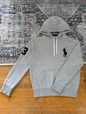 Ljusgrå Polo Ralph Lauren Hoodie Big Pony - Hej! 👋 Säljer en riktigt fräsch ljusgrå Polo Ralph Lauren ”Big Pony” hoodie i storlek M. Har den klassiska stora broderade loggan på bröstet och siffran ”3” på höger ärm. 🐎✨ Tröjan är i mycket gott skick, endast använd ett fåtal gånger så den känns som ny! 100% äkta med alla originaltvättlappar kvar (ingen QR-kod på denna modell). Ett perfekt och tidlöst lyxbasplagg! Fraktar snabbt! 💬 100% 🚛📦 