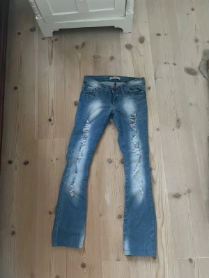 Blå slitna raka jeans - Snygga blå raka jeans från Crocker med slitningar och ljusa partier framtill. Låg midja och dragkedja. Perfekta för en trendig och avslappnad stil. 