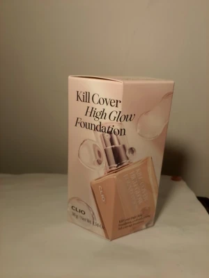 Clio Kill Cover High Glow Foundation - Clio Kill Cover High Glow Foundation i en fyrkantig glasflaska med pump. Färgen är ljus beige och ger en glowig finish. Förpackningen är stilren i ljusa toner och foundationen är flytande. Perfekt för dig som vill ha en naturlig lyster och jämn hudton.