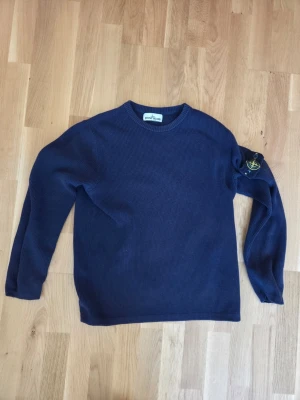 Stone Island tröja - Säljer en mörkblå stickad tröja från Stone Island med klassisk rund hals och lång ärm. Tröjan har den ikoniska Stone Island-loggan på vänster ärm. Perfekt för dig som gillar stilrena och trendiga plagg i mjukt material.