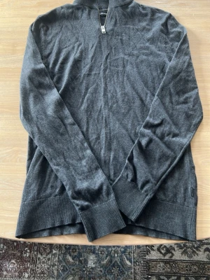 Mörkgrå halvzip tröja från Jack&jones  - Mörkgrå långärmad tröja från jack&jones med halvzip framtill. Tröjan har ribbade muddar vid ärmslut och nederkant. Perfekt för en stilren och avslappnad look.