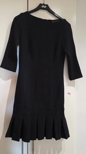 Svart klänning med plisserad nederdel - Stilren svart klänning från Zara Basic med trekvartsärm och plisserad nederdel. Klänningen har en klassisk, rak passform och är tillverkad i ett mjukt tyg som ger en elegant look. Perfekt för dig som gillar enkel men snygg design.