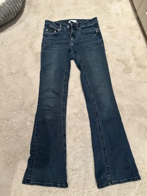 Blå bootcut jeans med mellanhög midja från Gina Tricot - Snygga blå bootcut jeans med klassisk femficksdesign och mellanhög midja. Jeansen har lätt tvättad look och utsvängda ben, perfekta för en avslappnad och trendig stil. Tillverkade i denim med stretch för extra komfort. Har knappt använt men fick hänga med i rensningen 