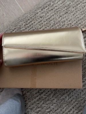 Guldig clutch - Guldig clutch som är använd en gång på min bal. Den har ett pyttelitet jack. Har ett par matchande klackar på min sida🫶🏻
