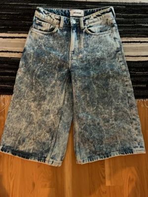 Acid wash jeansshorts från Weekday - Säljer ett par snygga acid wash jeansshorts från Weekday. De har en loose passform, klassisk femficksdesign och hög midja. Perfekta för dig som gillar en avslappnad och trendig stil. Materialet är bomull och färgen är en mix av blått och vitt.