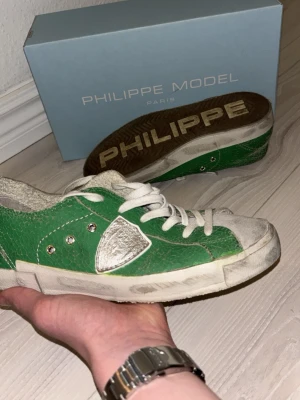 Gröna Philippe Model skor - Kan sänka pris vid snabb affär!Snygga gröna skor från Philippe Model med vita detaljer och vita skosnören. Skorna har en låg silhuett och är tillverkade i läder med silverfärgade metalldetaljer och en vit sula. Klassisk Philippe Model-logga på sidan och tydlig branding under sulan.