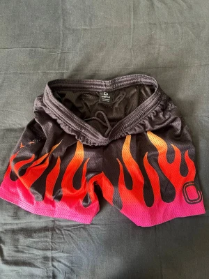 Overtime Fire Shorts – strl L - Säljer ett par Overtime Fire Shorts i flerfärgat Black / Red / Orange / Yellow / Pink mönster. Shorts är i 9/10 skick, sparsamt använda och i väldigt fint skick. Modellen har en kortare passform (kortare längd på benen) vilket ger en mer streetwear/basket-inspirerad look. Väldigt sköna och lätta shorts som funkar perfekt till både träning och vardag. • Skick: 9/10 • Färg: Black / Red / Orange / Yellow / Pink • Storlek: L • Passform: Kort (kortare benlängd) Kan skickas eller mötas upp beroende på