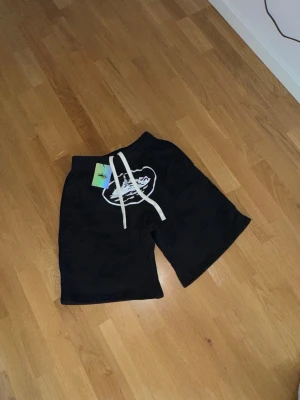 Svarta shorts från Corteiz - Säljer ett par svarta shorts från corteiz med vitt tryck framtill och vita dragsnören i midjan. Shortsen har elastisk midja och är gjorda i mjukt bomullsmaterial. Perfekta för en avslappnad streetwear-look.