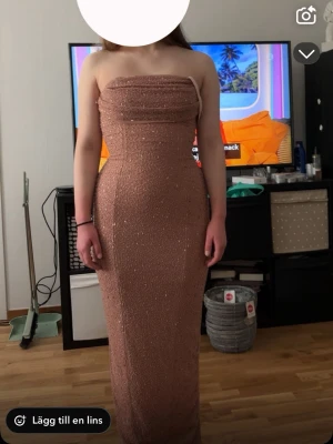 Glittrig axelbandslös långklänning - Säljer en snygg axelbandslös långklänning i en ljus beige ton med glittriga detaljer. Klänningen har figurnära passform, slits bak och är tillverkad i ett stretchigt syntetmaterial. Perfekt för bal eller festkvällar! Den är ifrån oh polly aldrig använd prislapp finns kvar. Finns inte oh polly i varumärke men den är därifrån. Köpt för 1600 