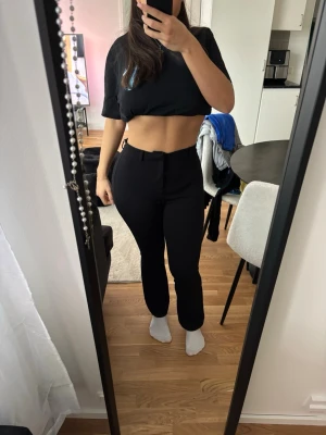 Svarta kostymbyxor med raka ben höga i midjan  - Säljer ett par svarta kostymbyxor med hög midja och raka ben. Byxorna har hysk- och hakstängning samt fickor i sidorna. Perfekta för en clean och stilren look. Materialet är slätt och stretchigt för extra komfort.