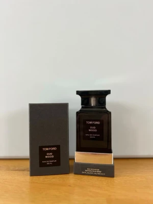 Tom Ford Oud Wood Eau de Parfum - Tom Ford Oud Wood Eau de Parfum är en exklusiv parfym i en elegant mörkbrun glasflaska med svart etikett och silverdetaljer. Flaskan har en stilren, fyrkantig form och rymmer 100 ml. Doften är känd för sina träiga och lyxiga noter, perfekt för dig som gillar unika och sofistikerade parfymer.
