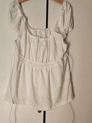 Vit sommarblus med knytband  - Söt vit blus med broderade detaljer, puffärmar och knytband i midjan. Blusen har en rundad halsringning och volangkant. Jag har nästan aldrig använt den och vill mest ba bli av med den