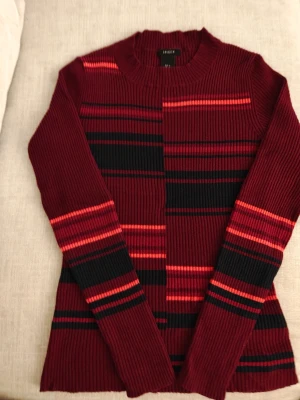 Randig vinröd stickad tröja Lindex - Stickad tröja från Lindex i vinrött med svarta och röda ränder. Tröjan har ribbad struktur, rund halsringning och långa ärmar. Perfekt för dig som gillar en färgstark och bekväm look.