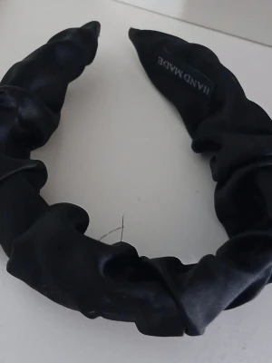 Svart satin diadem handgjort - Snyggt svart diadem i glansigt satinmaterial med scrunchie-effekt. Handgjort och perfekt för att ge en trendig touch till din look. Passar till både utsläppt hår och uppsättningar.