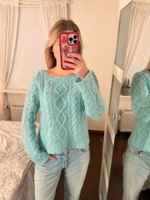 Ljusblå kabelstickad tröja - Mysig ljusblå stickad tröja med kabelstickat mönster framtill och på ärmarna. Tröjan har rund halsringning och långa ärmar. Perfekt för att hålla värmen under kyliga dagar och ger en avslappnad men ändå trendig look.