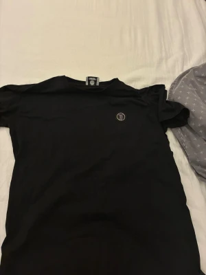 Svart Burberry t-shirt med logga - Svart t-shirt från Burberry med rund hals och en snygg broderad TB-logga på bröstet. Tillverkad i mjuk bomull och har en klassisk passform som funkar till det mesta. Perfekt för dig som gillar stilrena och exklusiva plagg.