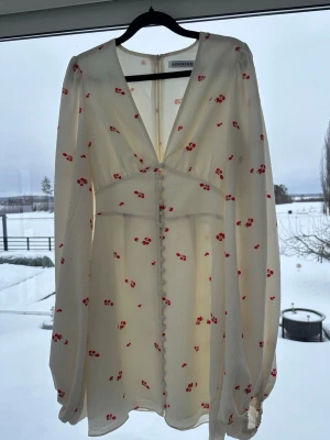 Florence dress från Adoore - Använd en gång, som ny! Vit miniklänning med rött blommönster från Adoore. Långa ärmar, v-ringning och markerad midja. Strl 34.
