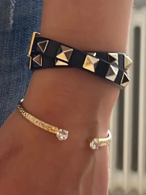 Svart valentino armband - Säljer ett svart läderarmband från Valentino med dubbla varv och coola guldfärgade pyramidnitar. Armbandet har ett stilrent spänne och kommer i original röd ask.