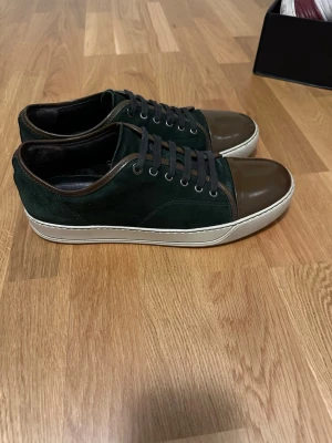 Mörkgröna lanvin skor - Snygga sneakers i mörkgrön mocka med bruna lackdetaljer på tån och runt kanten. Skorna har bruna skosnören och vit sula som ger en clean kontrast. Perfekta för dig som vill ha en unik och stilren look till vardagsoutfiten. Ingen box eller dustbag. 