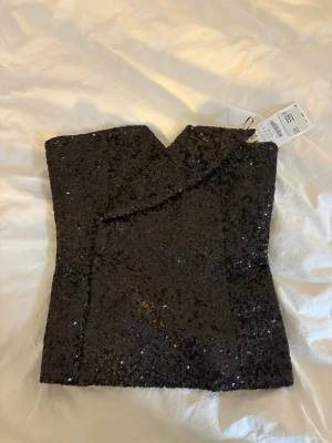 Off shoulder topp från Zara - Röd/brun korsettopp från Zara täckt med glittriga paljetter. Toppen är axelbandslös och har en dragkedja bak för enkel påklädning. Perfekt för dig som vill sticka ut med en trendig och festlig look. Storlek M, men passar även S!