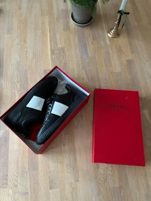 Valentino Garavani skor - Svarta sneakers från Valentino Garavani med en bred vit remsa över sidan. Klassisk låg modell med svarta snören och detaljerad sula. Snygg och stilren design som passar till det mesta. Kommer i original röd box. Lådan är lite skadad vilket syns på bilderna. Välldigt sköna skor och i nyskick
