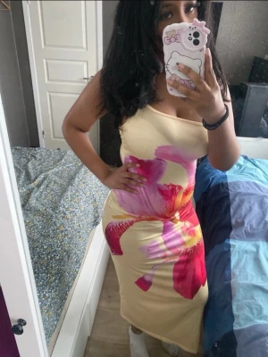 Blommig långklänning med smala axelband - Snygg långklänning i ljusgul nyans med stora blommiga mönster i rosa, rött och lila. Klänningen har smala axelband och figurnära passform, perfekt för sommarens varma dagar. Materialet känns mjukt och följsamt mot kroppen.