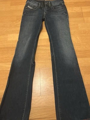 Blå bootcut jeans från Disel - Snygga blå bootcut jeans från disel med klassisk femficksdesign och slitningar på låren för en cool look. Jeansen är flare passform och är tillverkade i tåligt denimtyg som passar perfekt.