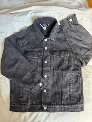 Svart jeansjacka från H&M - Snygg svart jeansjacka från H&M med rak passform, gråa knappar och två bröstfickor med lock. Jackan har även sidofickor och coola söm-detaljer. Storlek (S), skriv via dm vid funderingar 💬