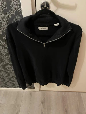 Svart stickad tröja med halvzip - Snygg svart stickad tröja från Jack & Jones med halvzip och hög krage. Tröjan har långa ärmar och ribbade muddar vid ärmslut och nederkant. Perfekt för lager på lager och enkel att matcha med olika outfits. Storlek S. 