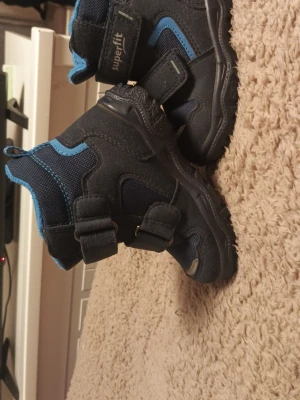 Kängor i strl 22 - Superfit kängor som är i färgerna mörkblå/svart med blå detaljer i storlek 22. Endast använda inomhus och i barnvagnen det vill säga att dom aldrig använts ute och därför så är dom i mycket fint skick med minimalt slitage. Smidiga och stadiga kängor med kardborreband som lätta att ta på och av. Rena och fräscha, redo för ny ägare. Skorna ligger även uppe på Vinted för samma pris.               ( Priset går att diskutera )