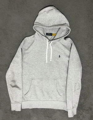 Grå hoodie från Polo Ralph Lauren - Snygg ljusgrå hoodie från Polo Ralph Lauren med klassisk logga broderad på bröstet. Bästa priserna här på Plick och skicka gärna in bud då jag kan sänka priset vid snabb affär.