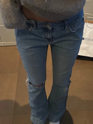 Levi's ljusblå bootcut jeans - Säljer ett par ljusblå Levi's jeans med bootcut passform och slitningar vid knäna. Klassisk femficksmodell med Levi's ikoniska röda etikett på bakfickan och läderpatch i midjan. Jeansen är i mjukt denimtyg och har en avslappnad vibe.