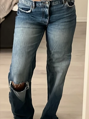 Blå ripped jeans från ZARA - Ett par blå jeans från ZARA med snygga slitningar och hål på benen. Klassisk femficksmodell med hög midja och raka ben. Jeansen har en cool, avslappnad vibe och är gjorda i denim med vintagekänsla.