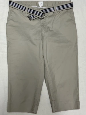 Beige shorts med randigt bälte Boomerang - Snygga beige shorts från Boomerang med ett randigt bälte i marinblått och vitt. Klassisk passform med fickor i sidorna och bälteshällor. Perfekta för en avslappnad och stilren look under varmare dagar.